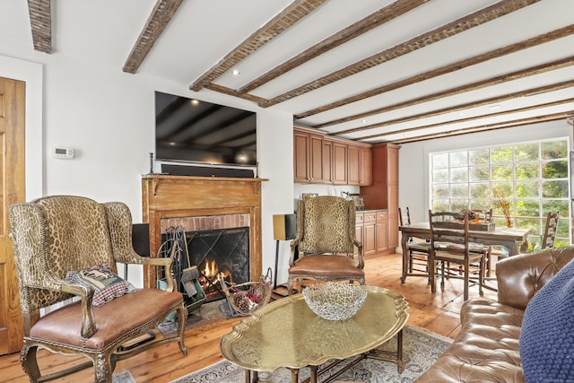 living area with beamed ceiling, light wood-style flooring, and a brick fireplace