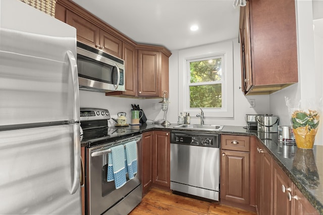 kitchen with stainless steel appliances, a sink, light wood-style floors, brown cabinets, and dark stone counters