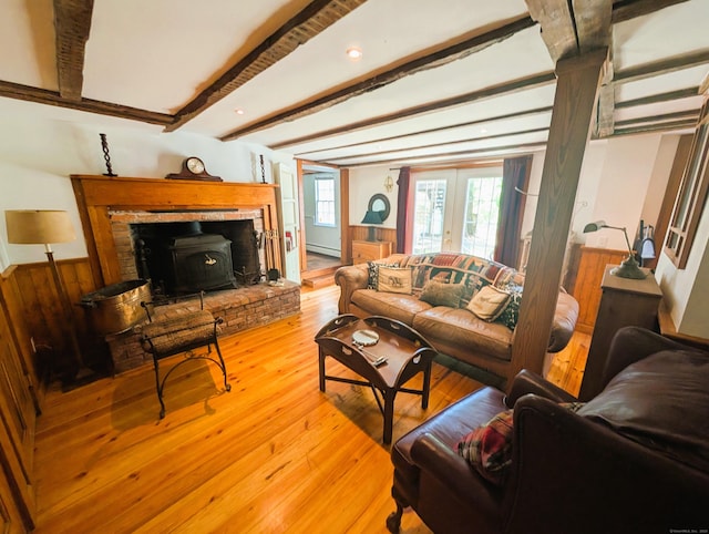 living room with a wood stove, a baseboard radiator, light wood-type flooring, beam ceiling, and french doors
