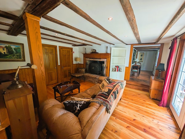 living area featuring beamed ceiling, light wood finished floors, and a fireplace with raised hearth