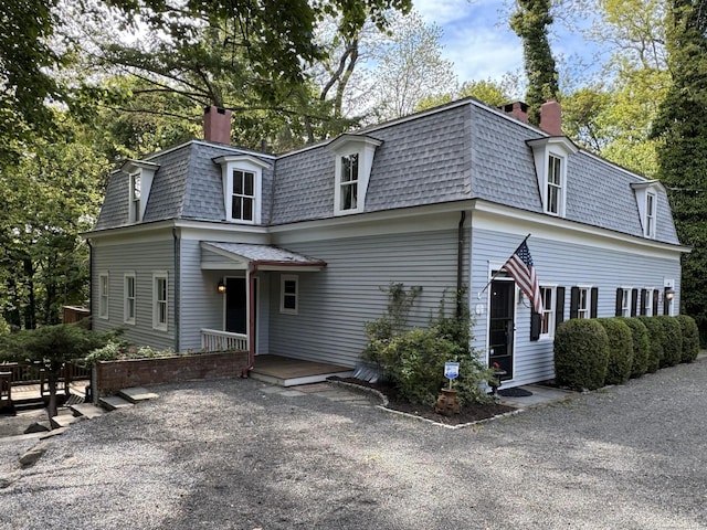 second empire-style home featuring mansard roof, a chimney, and a shingled roof