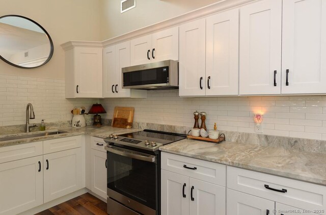 kitchen with appliances with stainless steel finishes, a sink, white cabinetry, decorative backsplash, and light stone counters