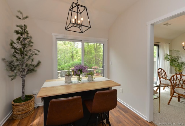 dining area featuring a chandelier, healthy amount of natural light, dark wood-type flooring, lofted ceiling, and baseboards