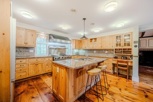 kitchen featuring wall chimney range hood, a sink, decorative backsplash, and a breakfast bar