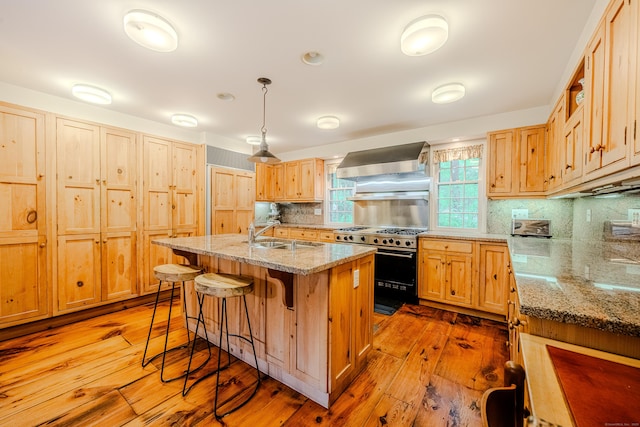 kitchen featuring high end stove, wall chimney exhaust hood, a sink, a breakfast bar, and light wood-style flooring