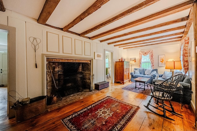 living room with light wood-type flooring, a fireplace, and beamed ceiling