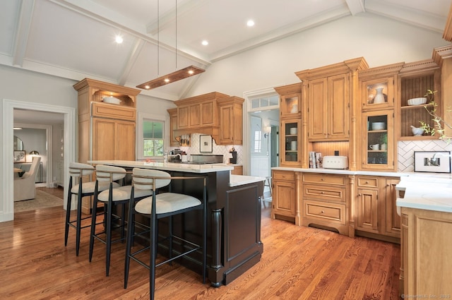 kitchen with beam ceiling, light countertops, open shelves, a center island with sink, and backsplash