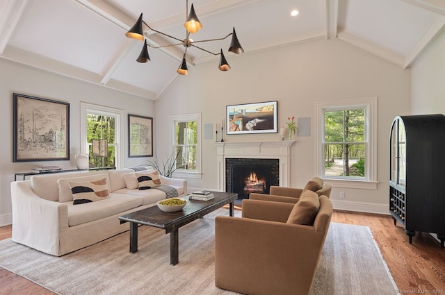living area with beam ceiling, light wood finished floors, a warm lit fireplace, high vaulted ceiling, and baseboards