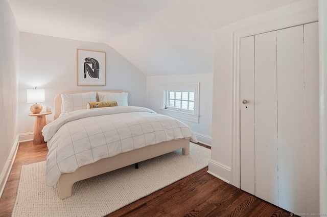 bedroom with wood finished floors, baseboards, vaulted ceiling, and a closet