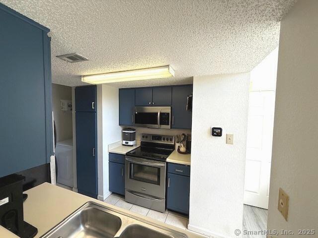 202 Carriage Crossing Ln Unit 202, Middletown, CT 06457 - kitchen with stainless steel appliances, blue cabinetry, a textured ceiling, light countertops, and washer / clothes dryer