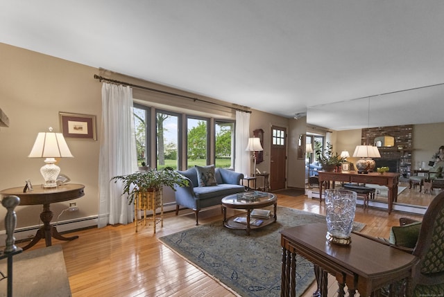 living area with light wood finished floors, a brick fireplace, and a baseboard heating unit