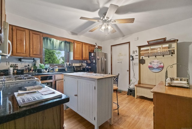 kitchen featuring freestanding refrigerator, brown cabinetry, light wood-type flooring, a ceiling fan, and a kitchen island