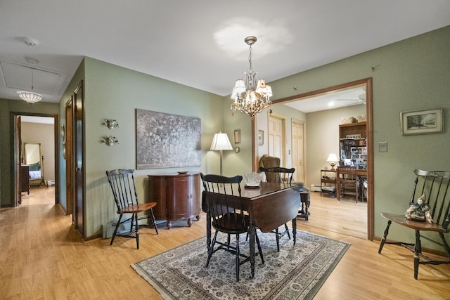 dining area featuring attic access, light wood-type flooring, baseboard heating, baseboards, and a chandelier
