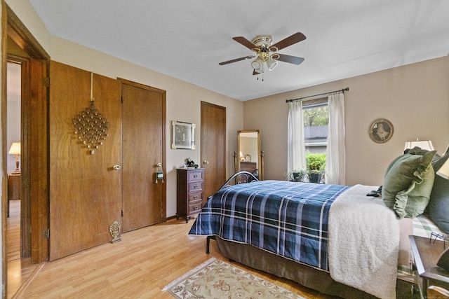 bedroom with two closets, light wood-style floors, and a ceiling fan