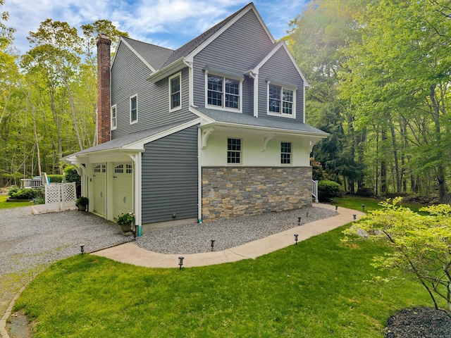 view of front of property featuring stone siding, an attached garage, a chimney, driveway, and a front yard