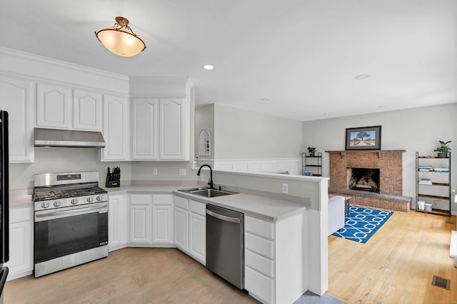 kitchen with stainless steel appliances, a sink, under cabinet range hood, a peninsula, and light countertops