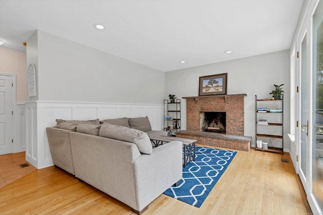 living area featuring a brick fireplace, wood finished floors, a wainscoted wall, and recessed lighting