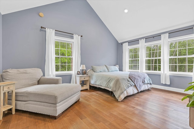 bedroom featuring multiple windows, light wood-style flooring, baseboards, and high vaulted ceiling