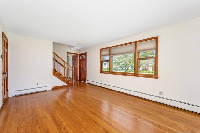 unfurnished living room with a baseboard heating unit, stairway, wood finished floors, and baseboards