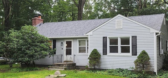 view of front facade featuring a chimney, roof with shingles, and a front lawn