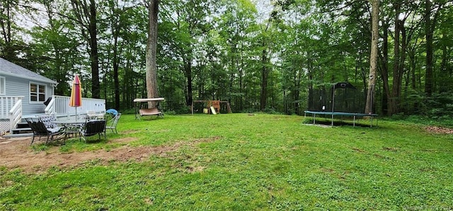 view of grassy yard with a trampoline and a deck