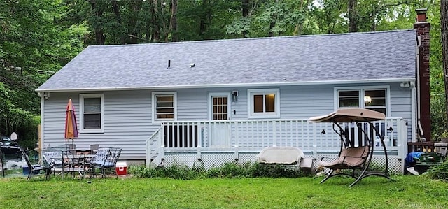 back of property with a shingled roof, a lawn, a wooden deck, and a chimney