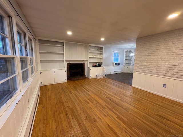 unfurnished living room featuring wood finished floors, a brick fireplace, a wainscoted wall, built in features, and brick wall
