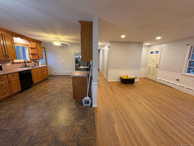 kitchen with dishwasher, a sink, brown cabinetry, baseboard heating, and a wainscoted wall