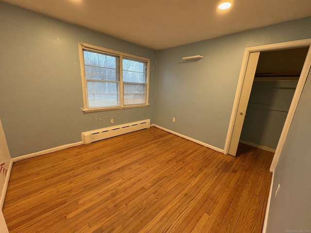 unfurnished bedroom with a baseboard radiator, wood finished floors, recessed lighting, baseboards, and a closet