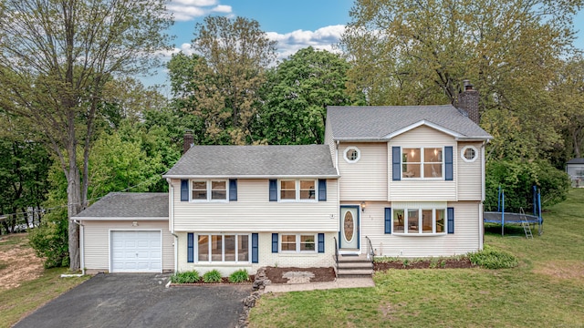 tri-level home with a garage, a chimney, asphalt driveway, a front yard, and a trampoline