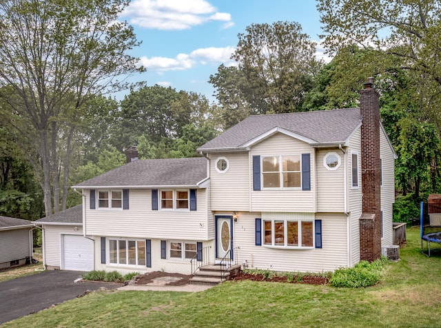 tri-level home featuring a trampoline, a chimney, driveway, and a shingled roof