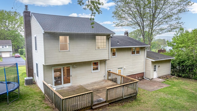 back of property with a trampoline, a chimney, cooling unit, and a lawn