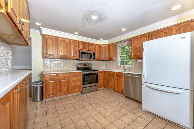 kitchen featuring stainless steel appliances, crown molding, light countertops, brown cabinetry, and a sink