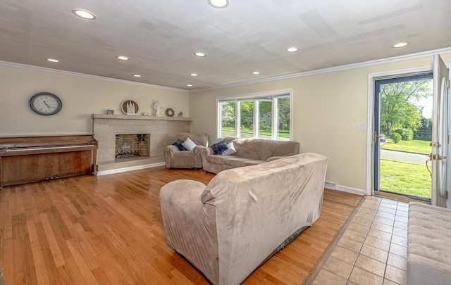 living area featuring ornamental molding, plenty of natural light, recessed lighting, a fireplace with raised hearth, and light wood-style floors