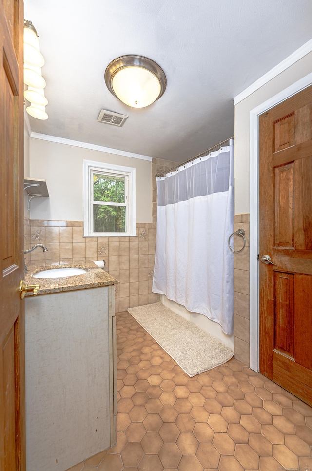 bathroom with tile walls, a shower with shower curtain, vanity, ornamental molding, and a wainscoted wall