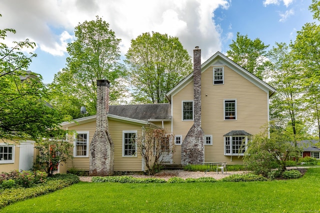 rear view of property featuring a chimney and a lawn