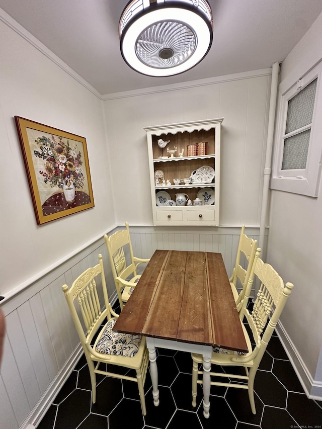 dining space with tile patterned floors, a decorative wall, ornamental molding, and wainscoting