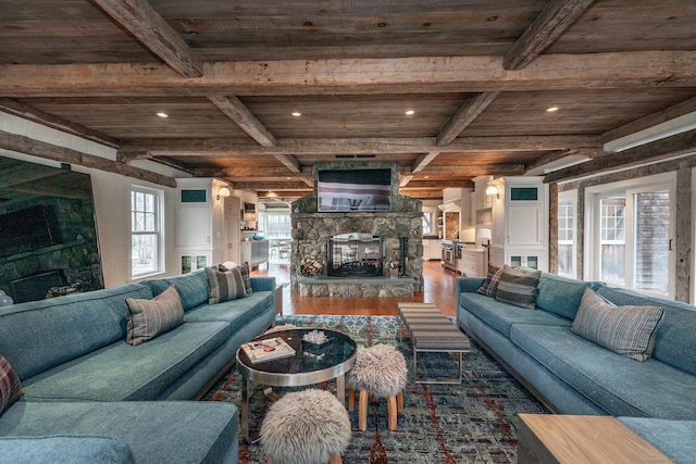 living area with a stone fireplace, wooden ceiling with exposed beams, wood finished floors, and recessed lighting