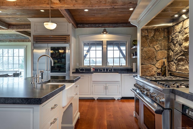 kitchen featuring high end appliances, wood ceiling with exposed beams, a sink, dark countertops, and dark wood finished floors