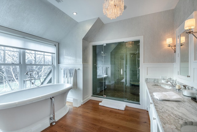 bathroom with a stall shower, wainscoting, vaulted ceiling, double vanity, and a decorative wall