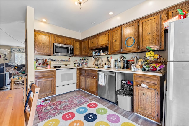 kitchen with stainless steel appliances, light countertops, brown cabinets, a sink, and recessed lighting