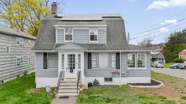colonial inspired home with solar panels, a chimney, a shingled roof, a front yard, and entry steps