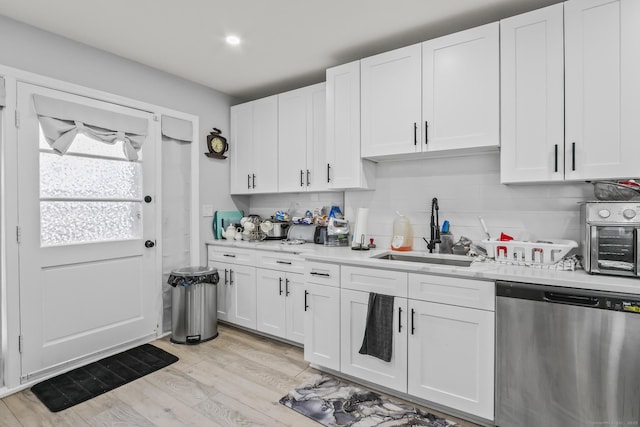kitchen featuring dishwasher, a sink, light countertops, backsplash, and white cabinetry
