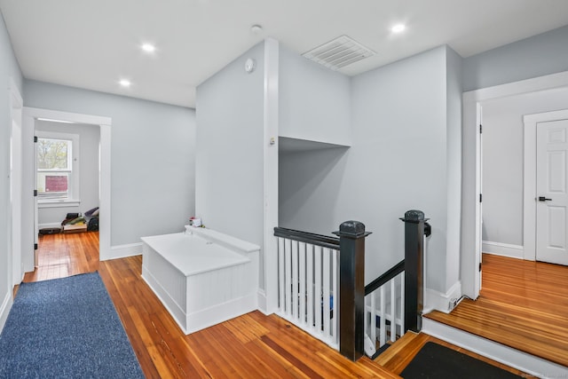 hall with an upstairs landing, hardwood / wood-style floors, recessed lighting, and baseboards