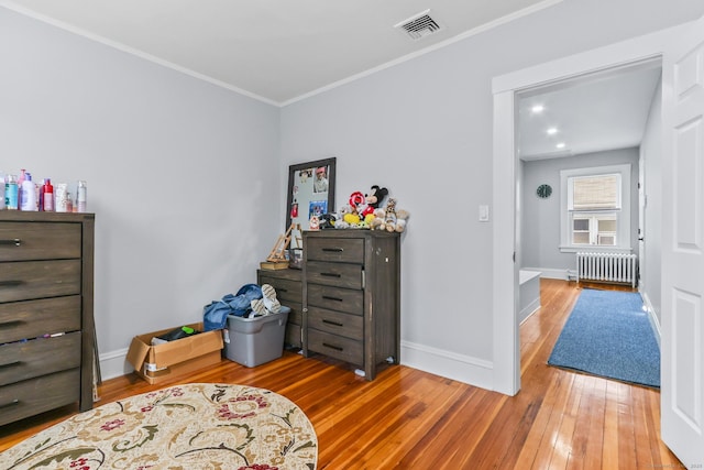 bedroom with radiator heating unit, hardwood / wood-style flooring, crown molding, and baseboards