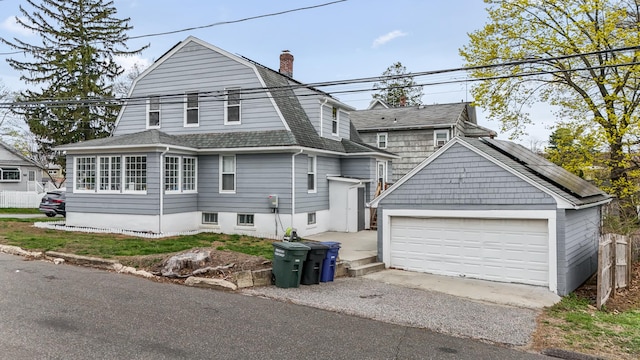 view of front facade featuring a chimney, a gambrel roof, solar panels, a shingled roof, and fence