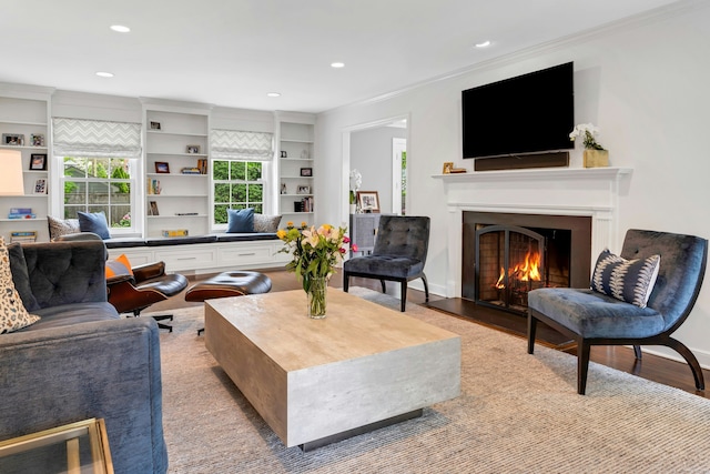 living area with crown molding, a warm lit fireplace, recessed lighting, and light wood-style flooring