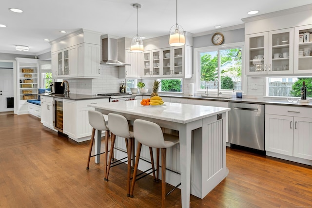 kitchen with stainless steel dishwasher, a sink, crown molding, wall chimney range hood, and decorative backsplash