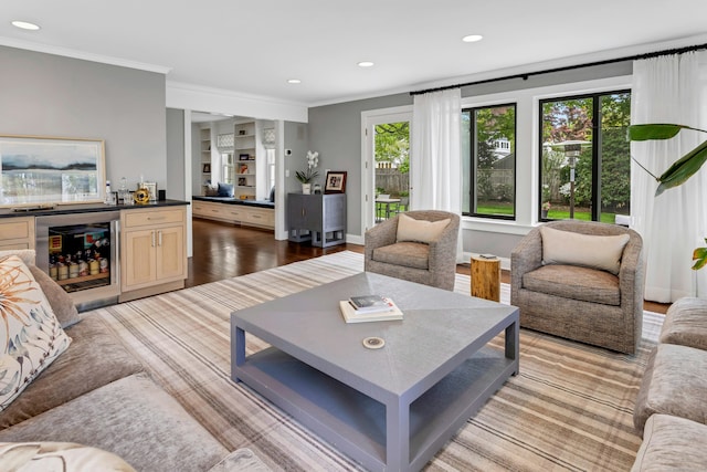 living room featuring beverage cooler, ornamental molding, recessed lighting, wood finished floors, and bar