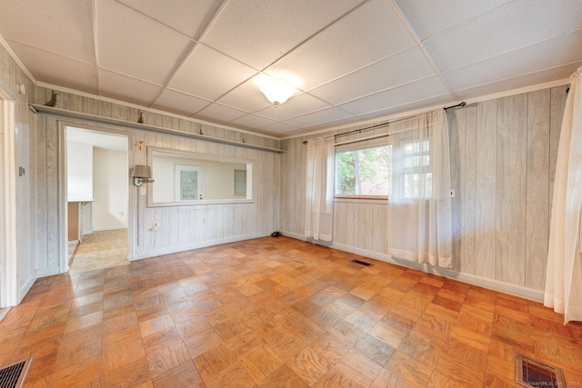 unfurnished room featuring baseboards, wooden walls, and a paneled ceiling